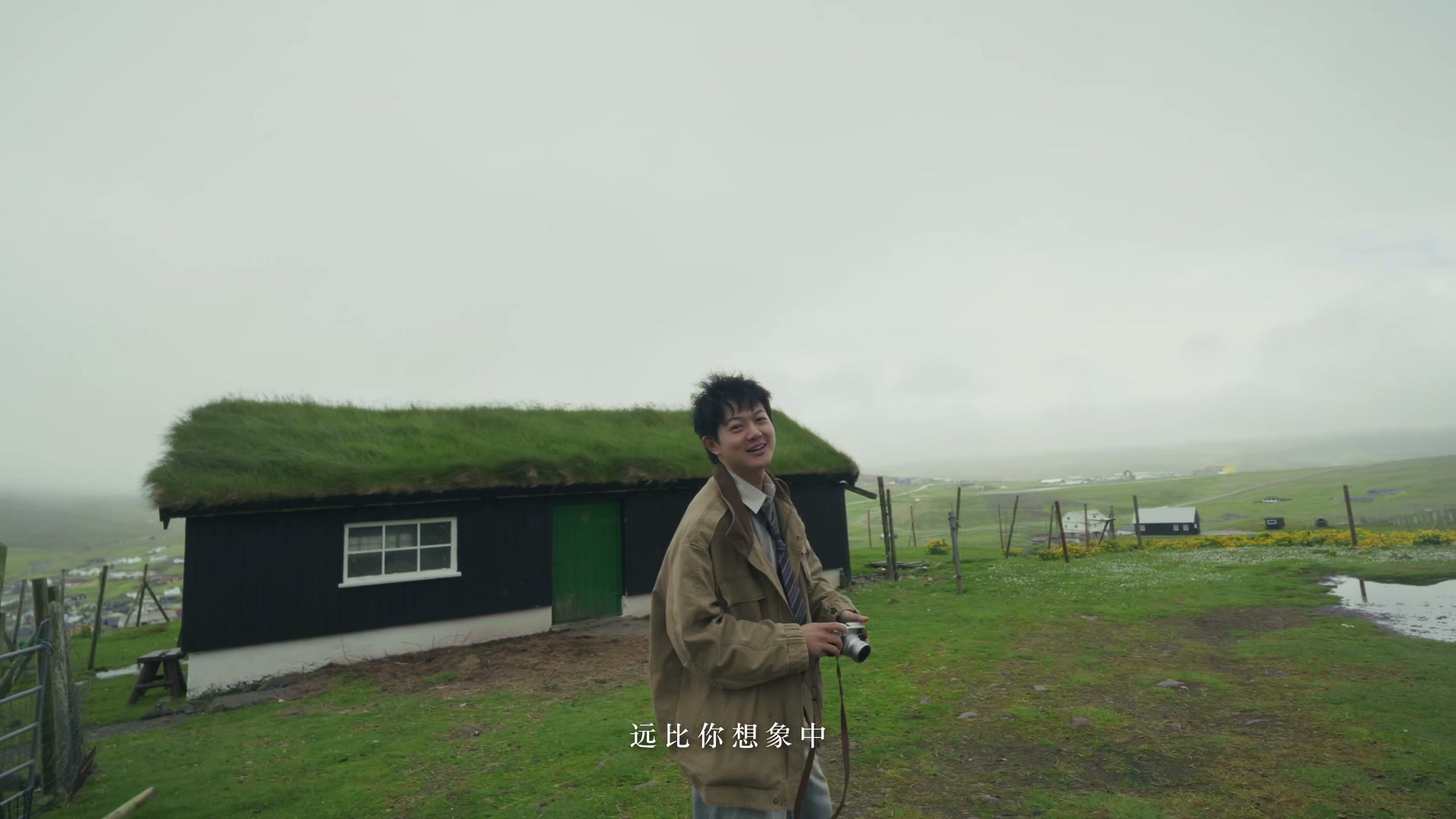 Traveller holding a camera beside a grass-roof house in the Faroe Islands